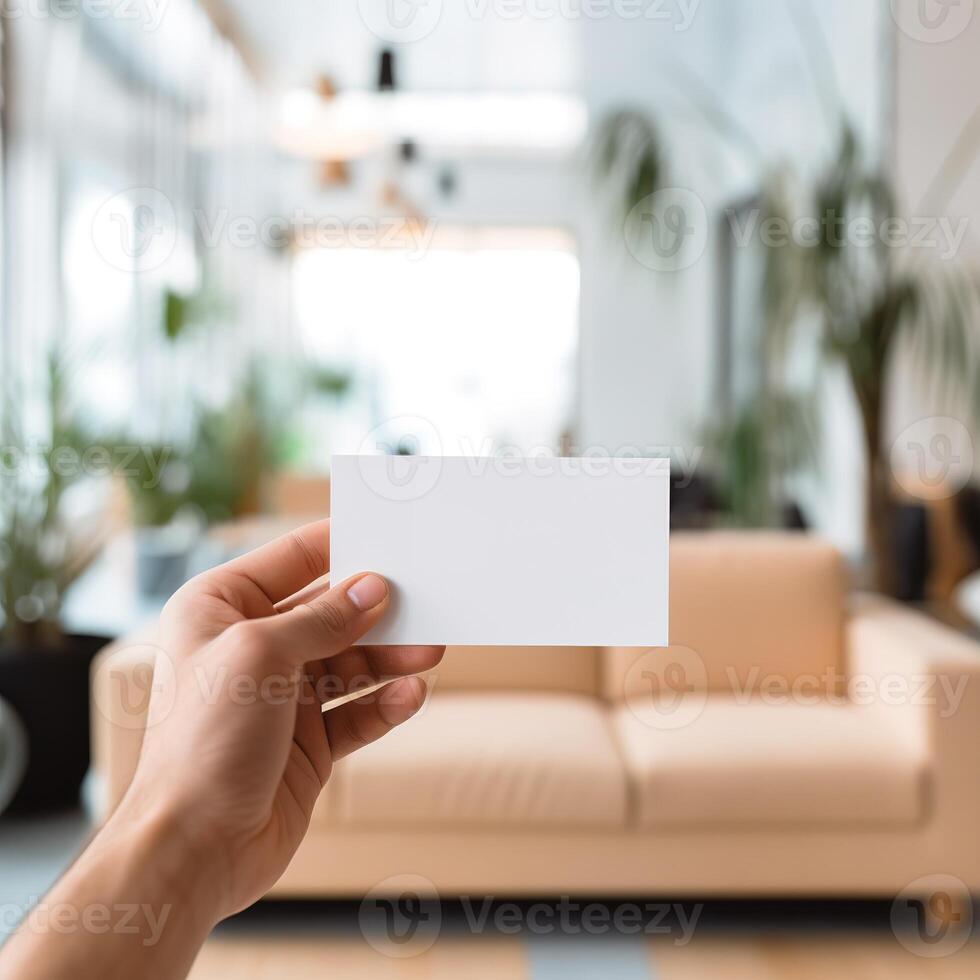 a hand holding a business card in front of a living room photo