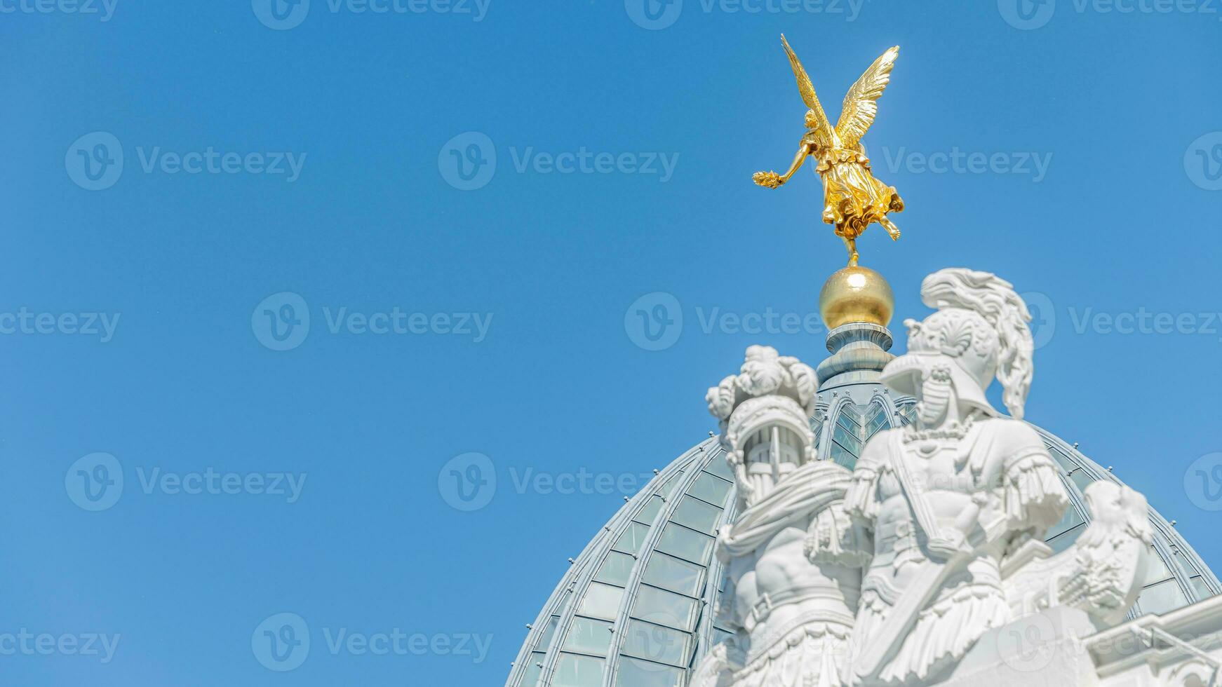 Dresden, Germany -Banner with old statue of a golden angel and warriors and knights at the dome top in downtown of Dresden, with copy space blue sky solid background. photo