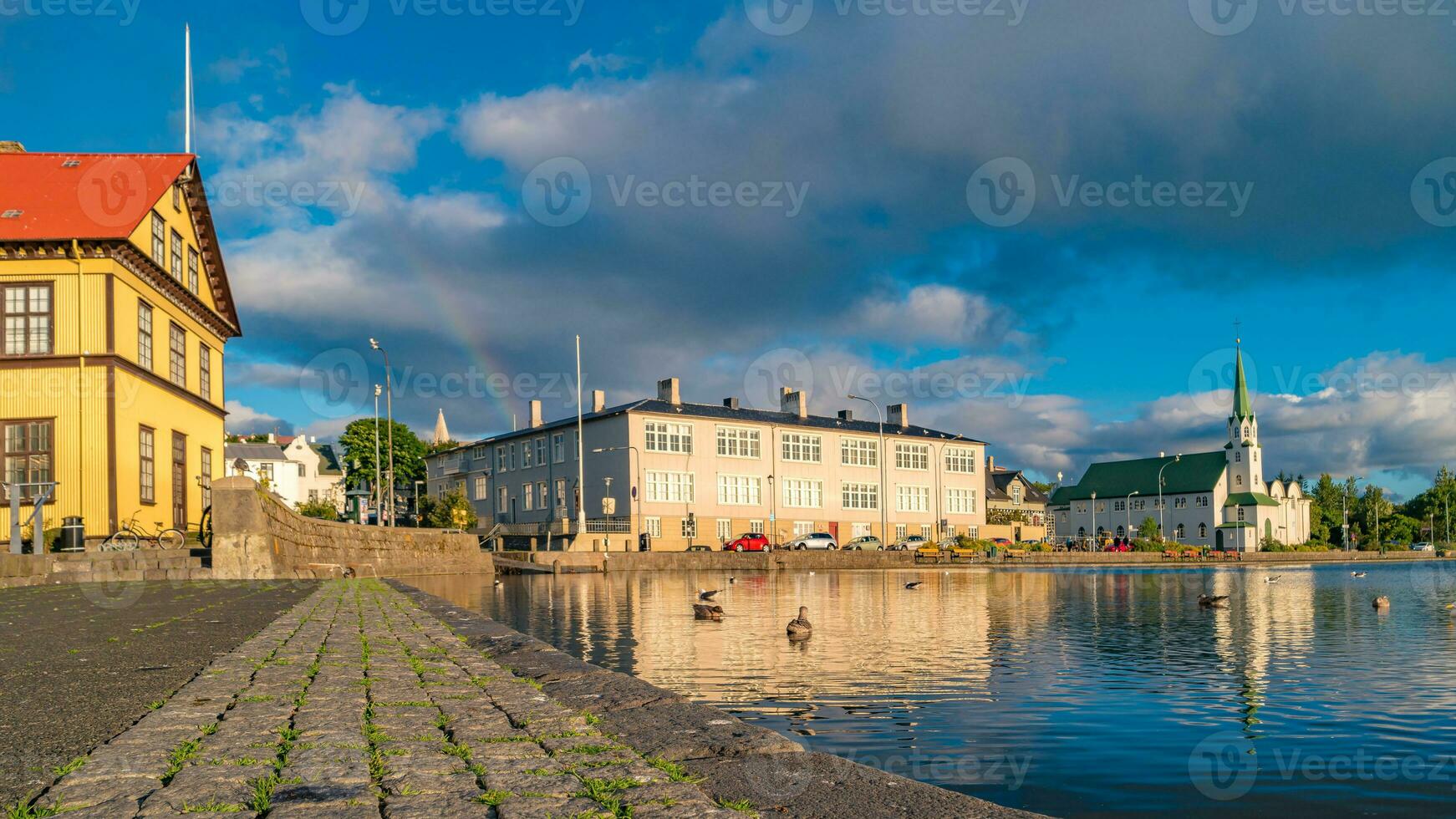 Historical and touristic downtown in Reykjavik at sunset and rainbow in Iceland. Cityscape at golden hour and blue sky at inner lake around Tjornin city park in the downtown. photo