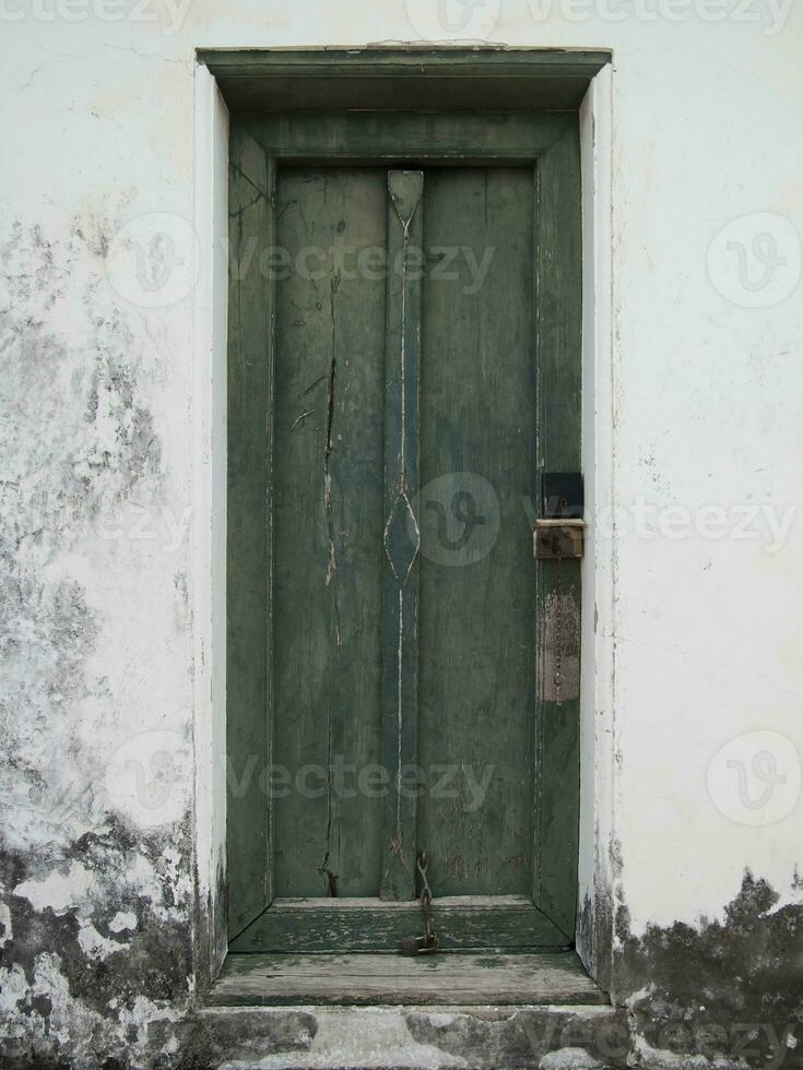 Antique green wooden door on the white old wall photo