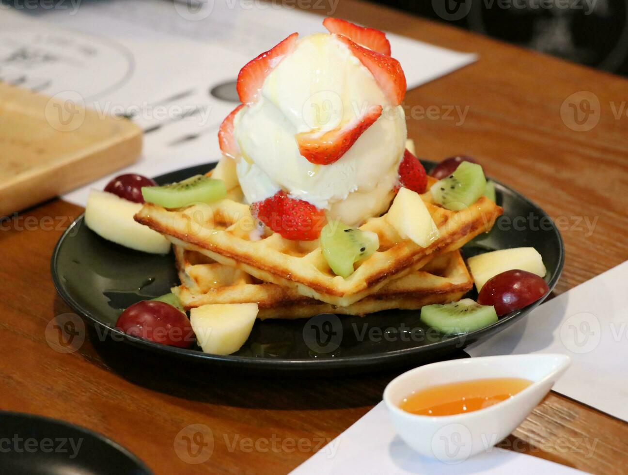 Ice cream on top of wafers and toppings with fruit such as strawberries, kiwi, grapes, and apples photo