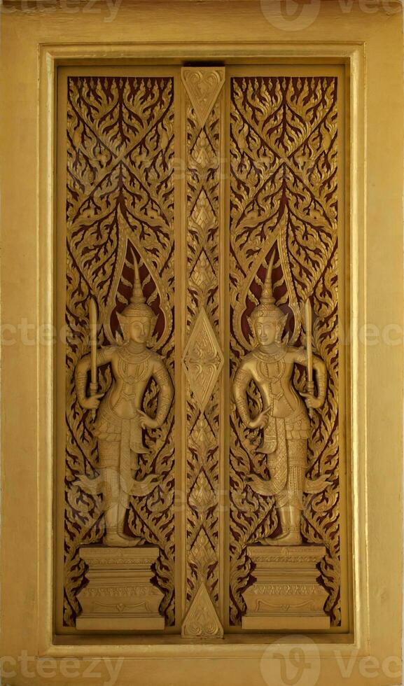 The golden wooden temple door is carved with two deities and exquisite ancient Thai patterns. Decorations at the entrance to the church photo