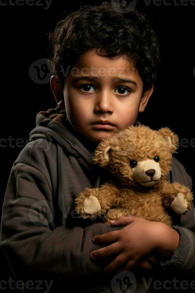 Grieving immigrant boy clutching worn teddy bear isolated on a gray gradient background photo
