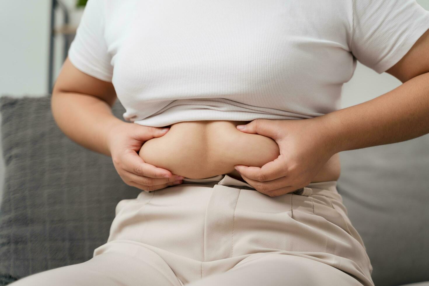 Close up of chubby woman holding her belly fat on the sofa. Diet lifestyle to reduce belly and shape up healthy, abdominal muscle concept. photo