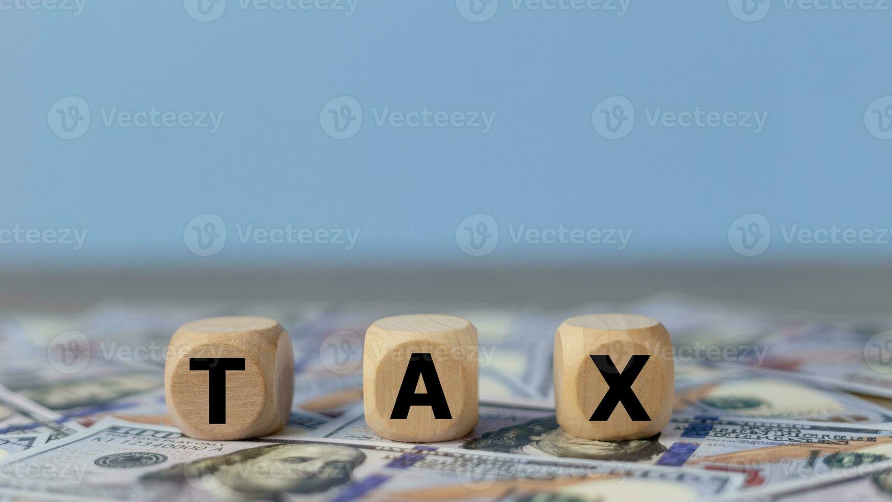 Tax word on wooden cubes on the background of dollar banknotes. Tax payment reminder or annual taxation concept. photo