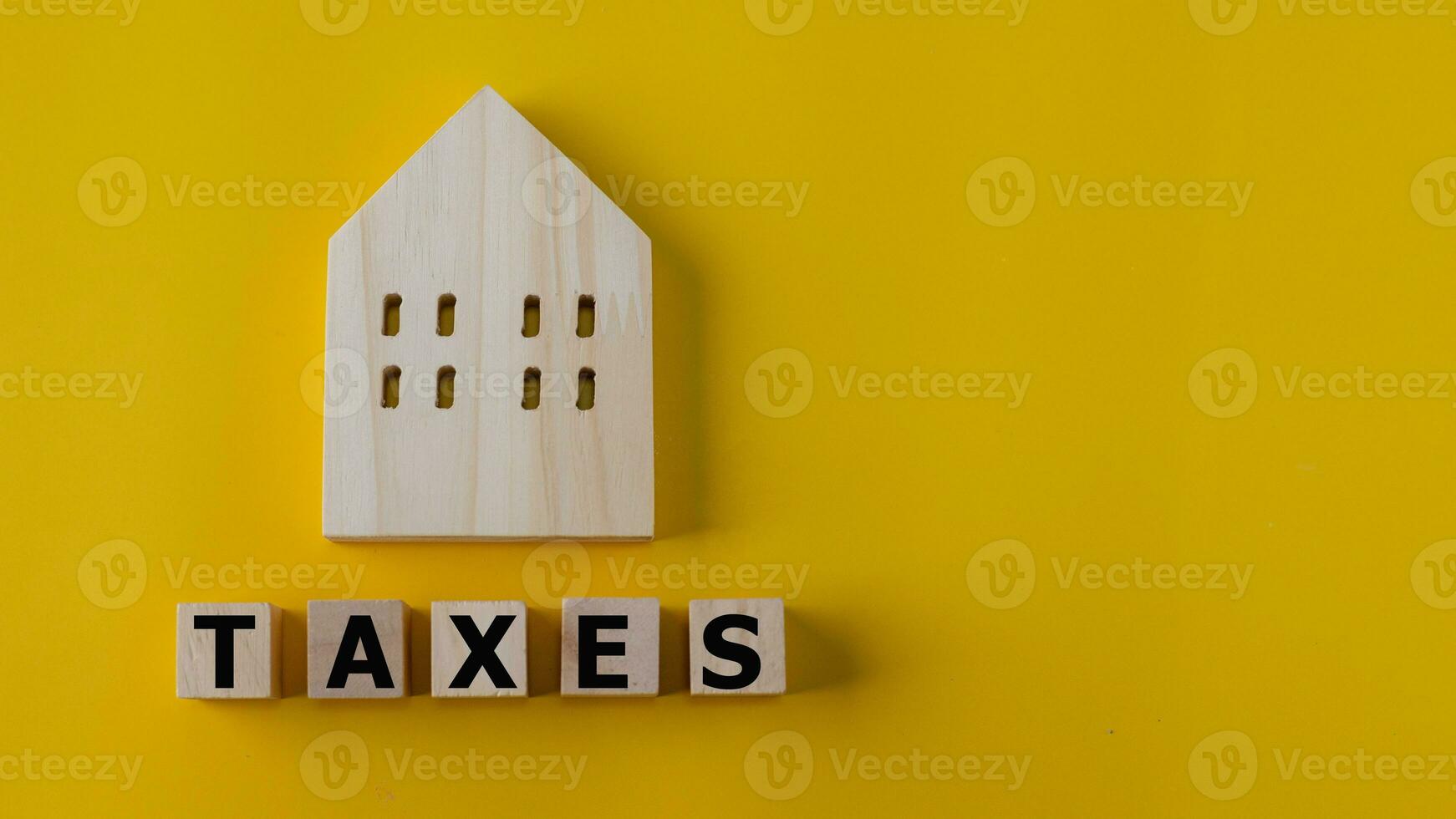Property tax concept. investment planning.Wooden blocks with the word TAXES and a house on a yellow background. photo