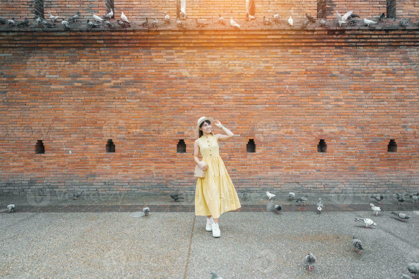 joven asiático mujer viajero en amarillo vestir con sombrero y bolso de viaje en eso pae puerta, turista visitar a el antiguo ciudad en chang Mai, tailandia Asia viajar, vacaciones y verano fiesta concepto foto