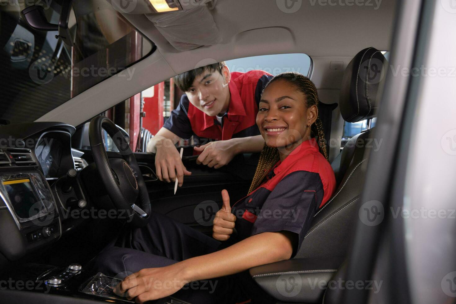 Young Black female automotive mechanic technician and partner check maintenance list in car interior at garage with smiles. Vehicle service fix and repair works, industrial occupation business jobs. photo