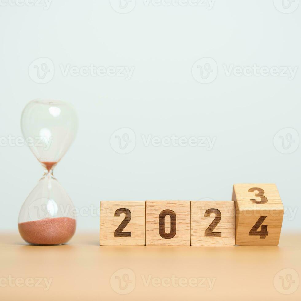 flipping block 2023 to 2024 text with hourglass on table. Resolution, time, plan, goal, motivation, reboot, countdown  and New Year holiday concepts photo