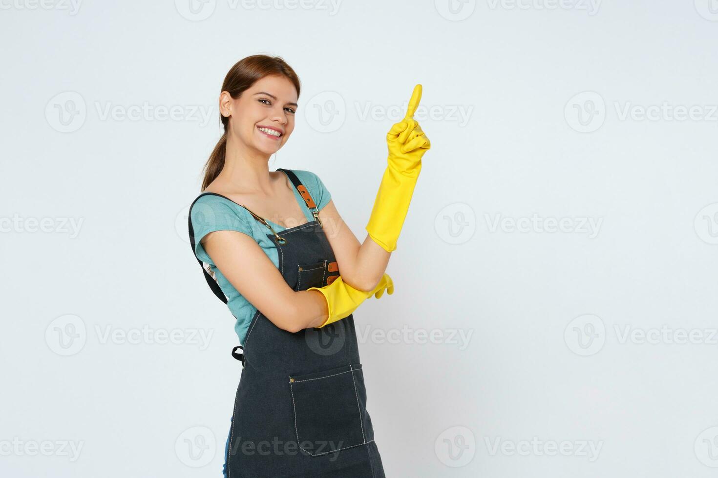 joven mujer vistiendo amarillo caucho guantes para manos proteccion y señalando a vacío Copiar espacio aislado en blanco antecedentes. foto