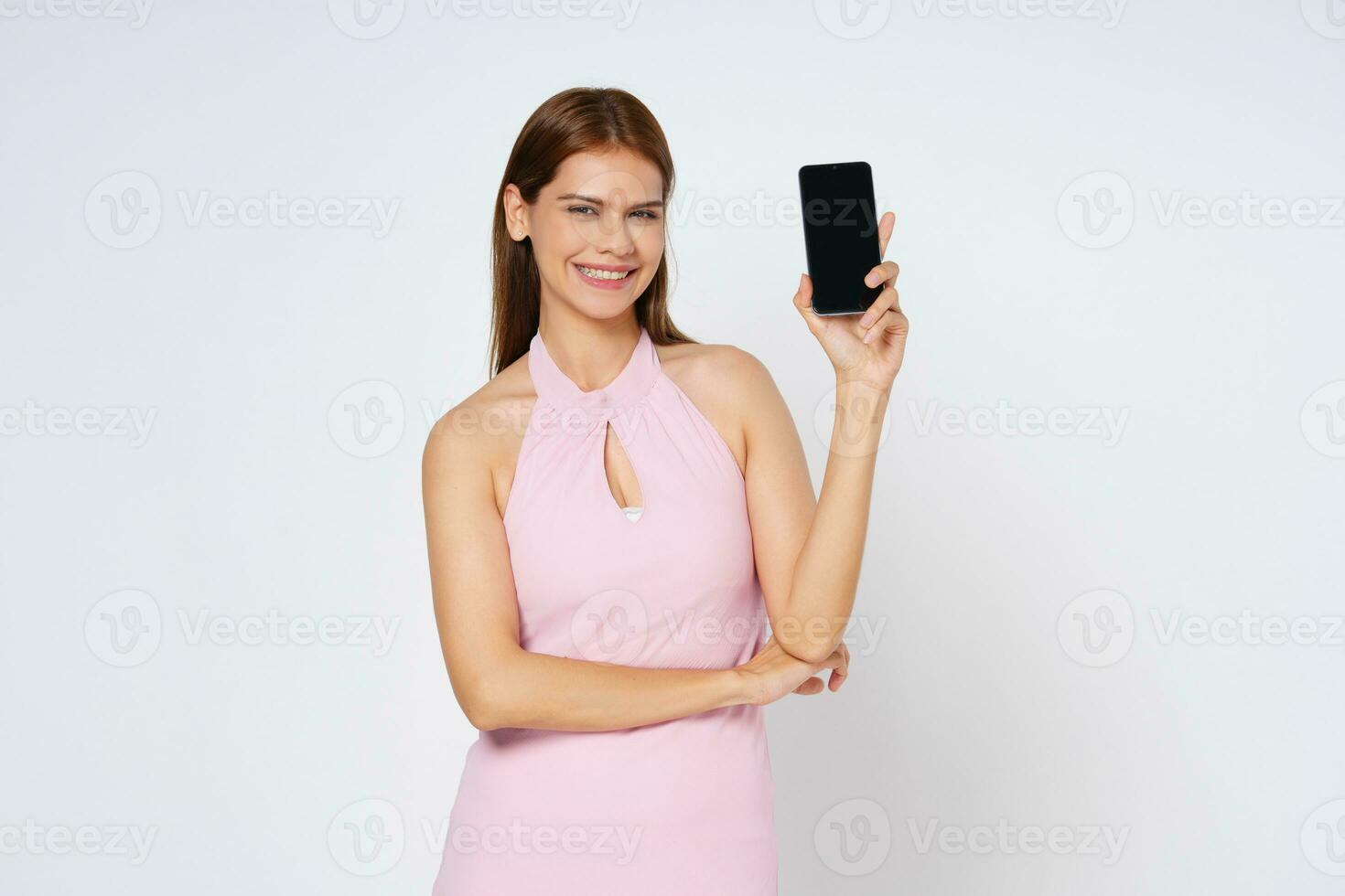 Smiling young woman holding mobile phone while standing isolated over white background. photo