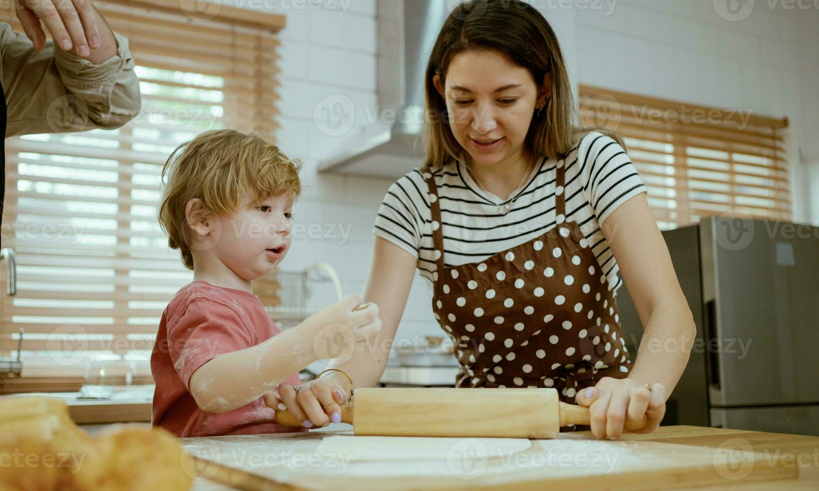 padre y madre enseñando bebé hijo amasadura masa en cocina mostrador a hogar. padres y chico niño disfrutar y divertido adentro actividad Cocinando juntos. foto