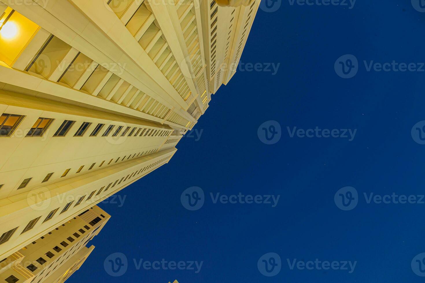 Vertical shot from bottom to top of illuminated skyscraper against blue sky photo