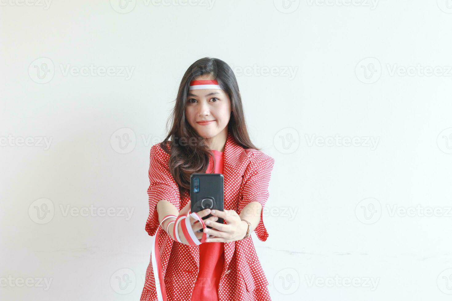 portrait of beautiful asian woman wearing red outfit celebrating Indonesia independence day holding mobile phone and smiling photo