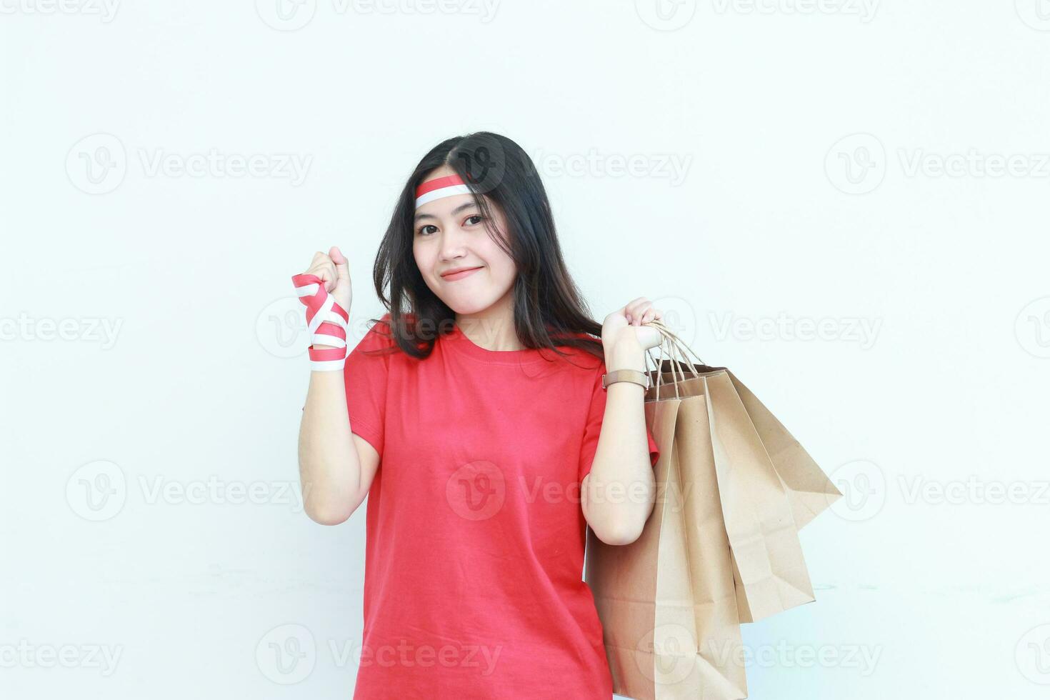 retrato de hermosa asiático mujer vistiendo rojo atuendo celebrando Indonesia independencia día por gesticulando que lleva un montón de compras pantalones con contento expresión foto