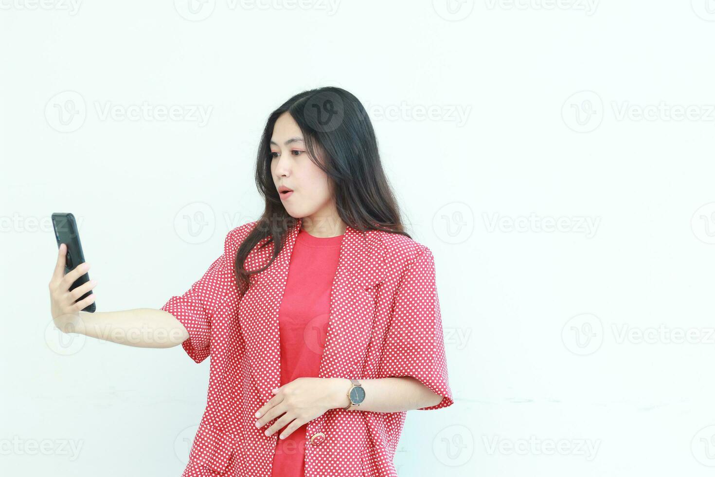 portrait of beautiful asian woman wearing red outfit looking at mobile phone with surprised expression photo