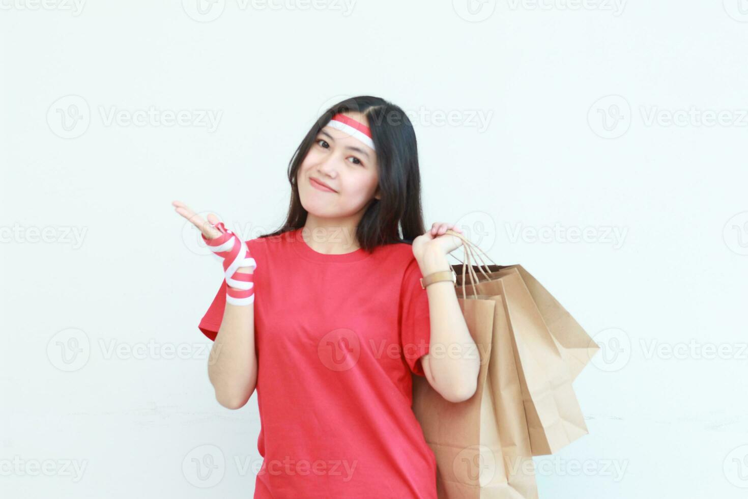 retrato de hermosa asiático mujer vistiendo rojo atuendo celebrando Indonesia independencia día por gesticulando que lleva un montón de compras pantalones con contento expresión foto