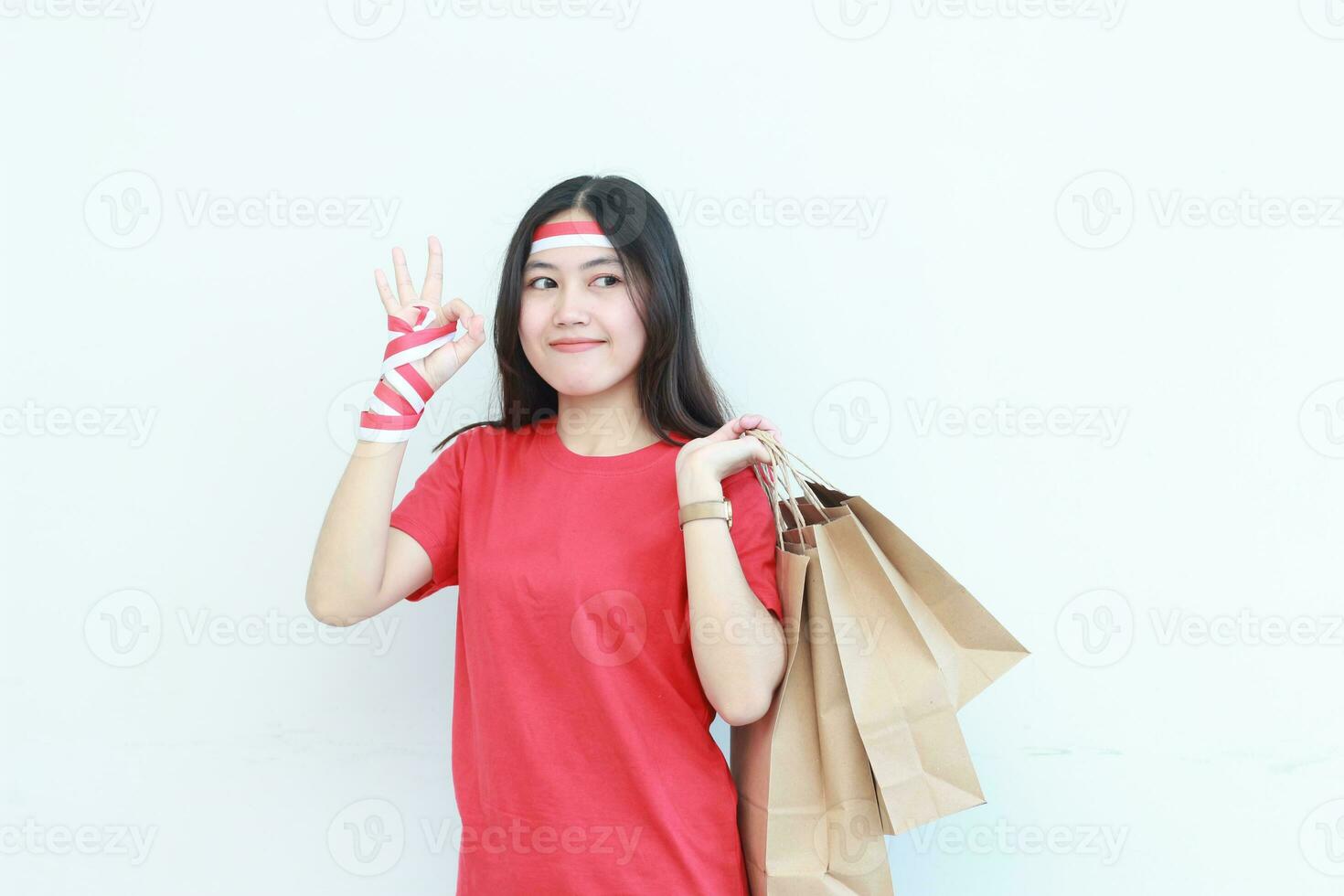 retrato de hermosa asiático mujer vistiendo rojo atuendo celebrando Indonesia independencia día por gesticulando que lleva un montón de compras pantalones con contento expresión foto