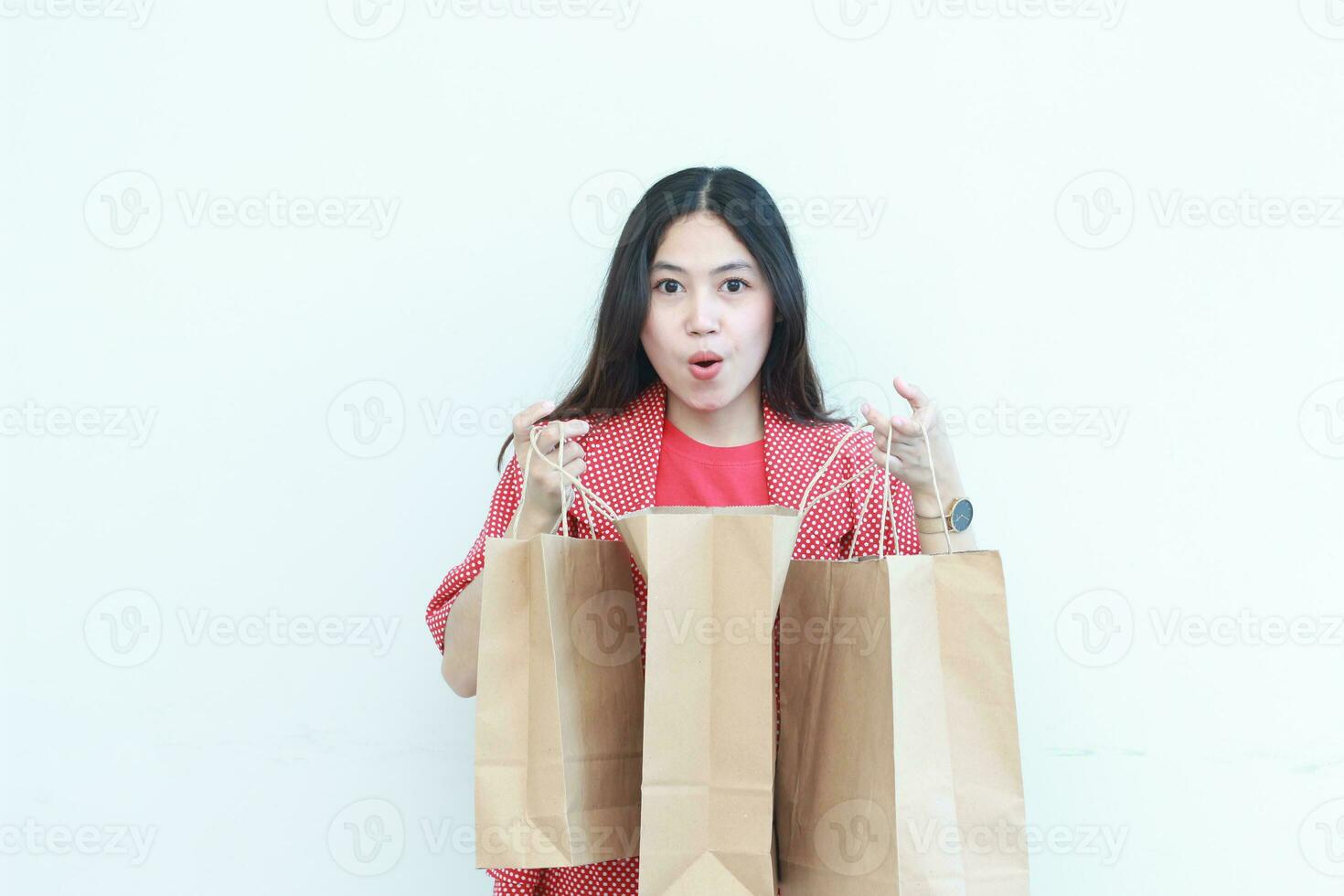 portrait of beautiful asian woman wearing red outfit with surprised gesture looking at contents of shopping bag photo
