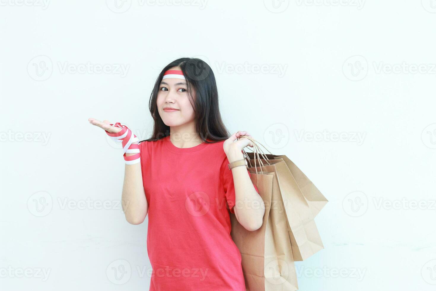 retrato de hermosa asiático mujer vistiendo rojo atuendo celebrando Indonesia independencia día por gesticulando que lleva un montón de compras pantalones con contento expresión foto