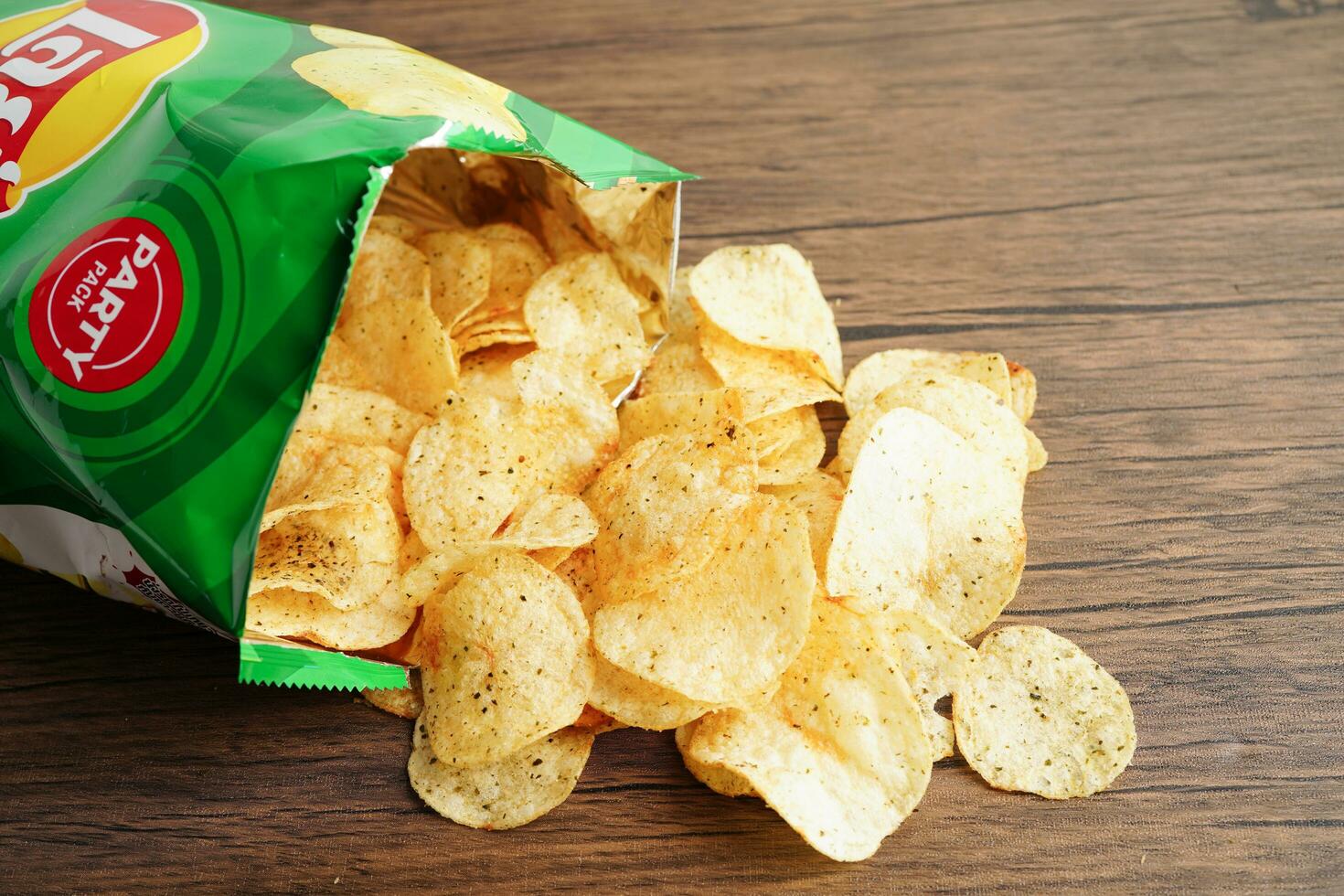 Bangkok, Thailand - May 15, 2022 Potato chips in open bag, delicious BBQ seasoning spicy for crips, thin slice deep fried snack fast food in open bag. photo