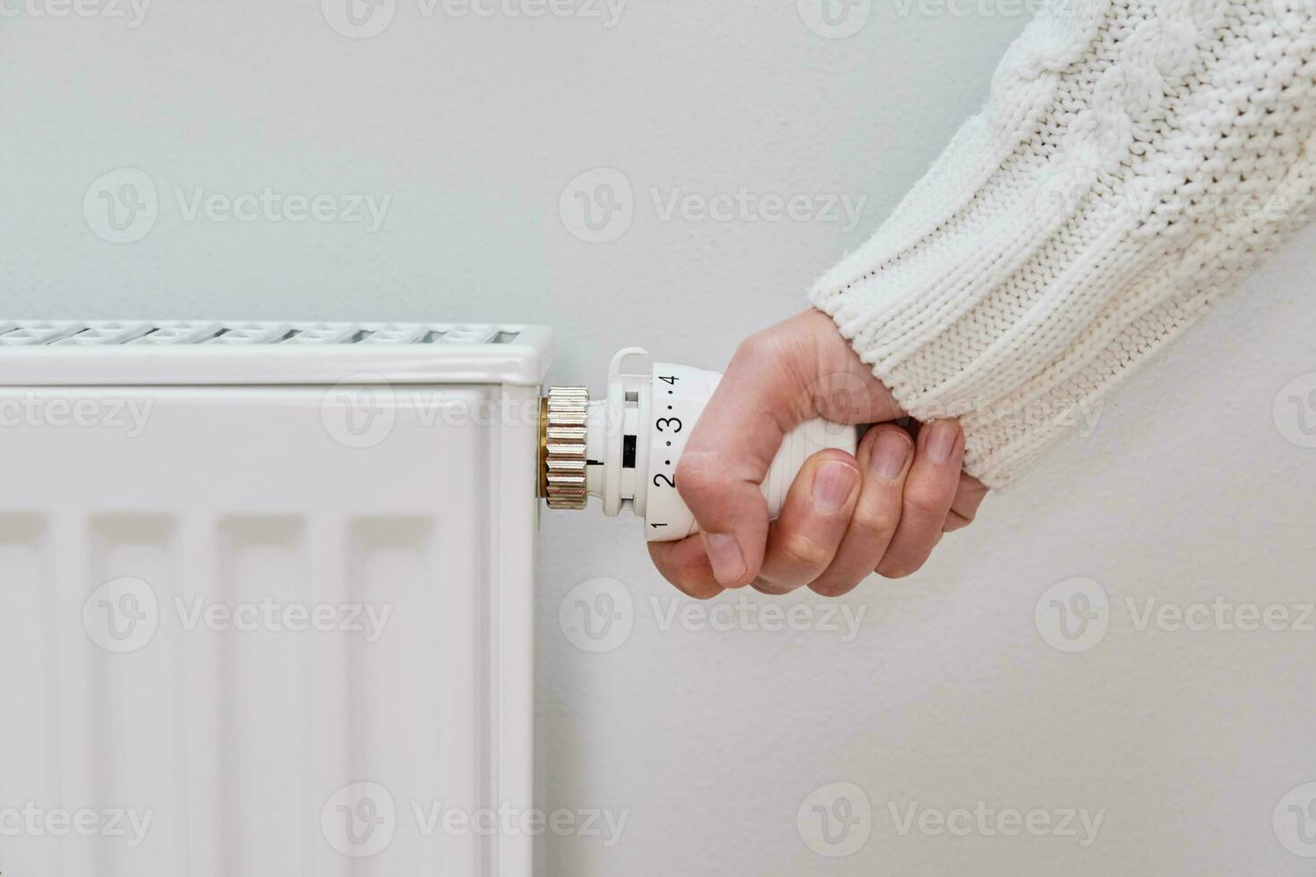 Woman in warm sweater adjusting temperature on heating radiator photo