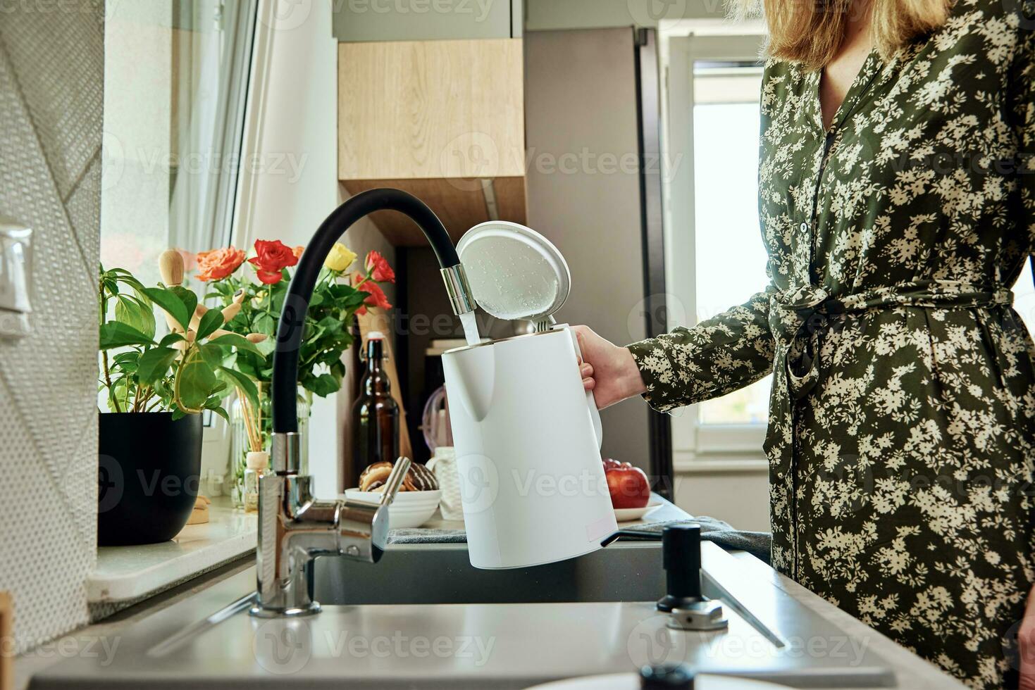 Woman pouring water from faucet into electric kettle at the kitchen photo