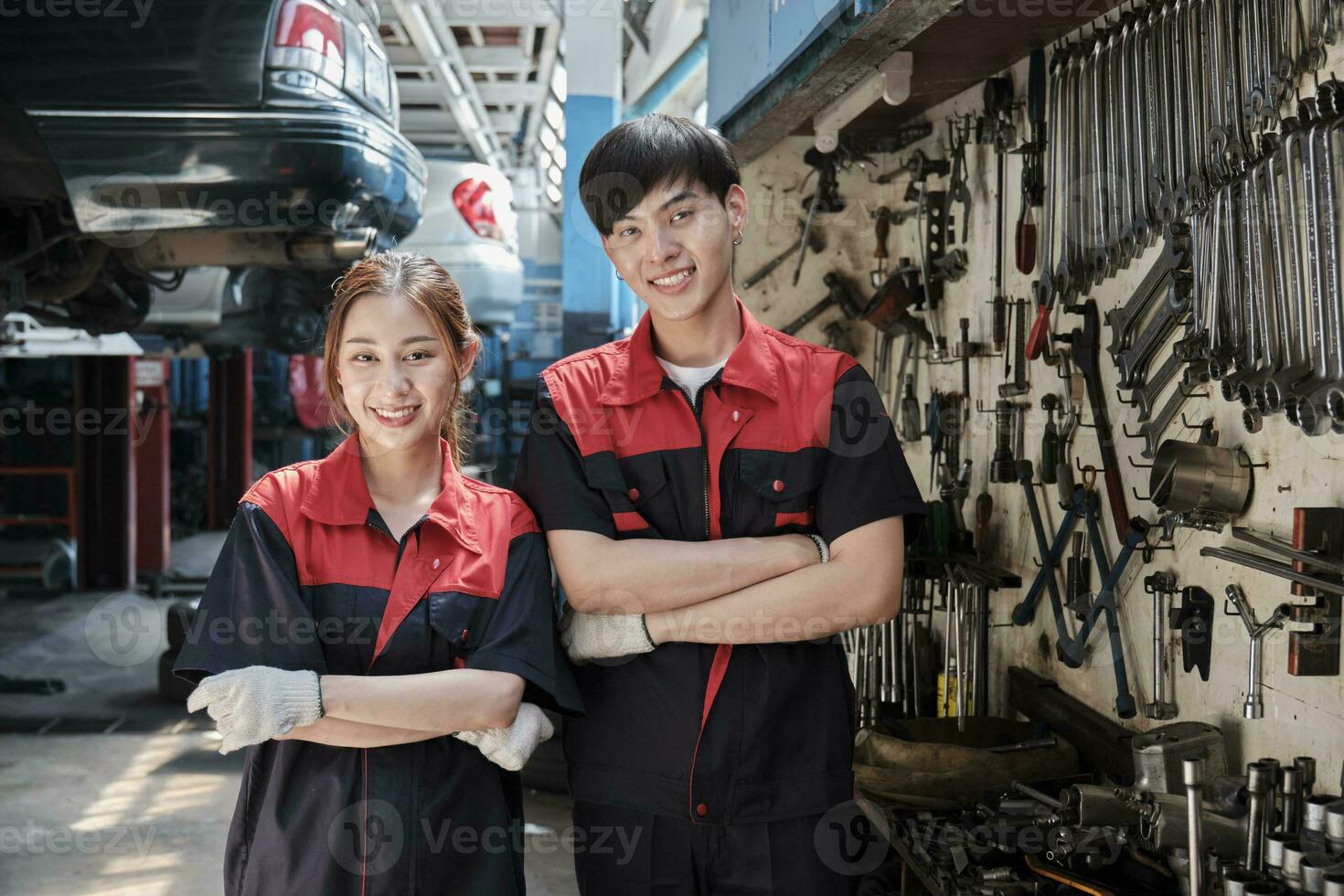 Portrait of two professional Asian mechanic partners smile and arms crossed with hand tools machinery, fixing work at car service garage, maintenance and repair jobs in automotive industry business. photo