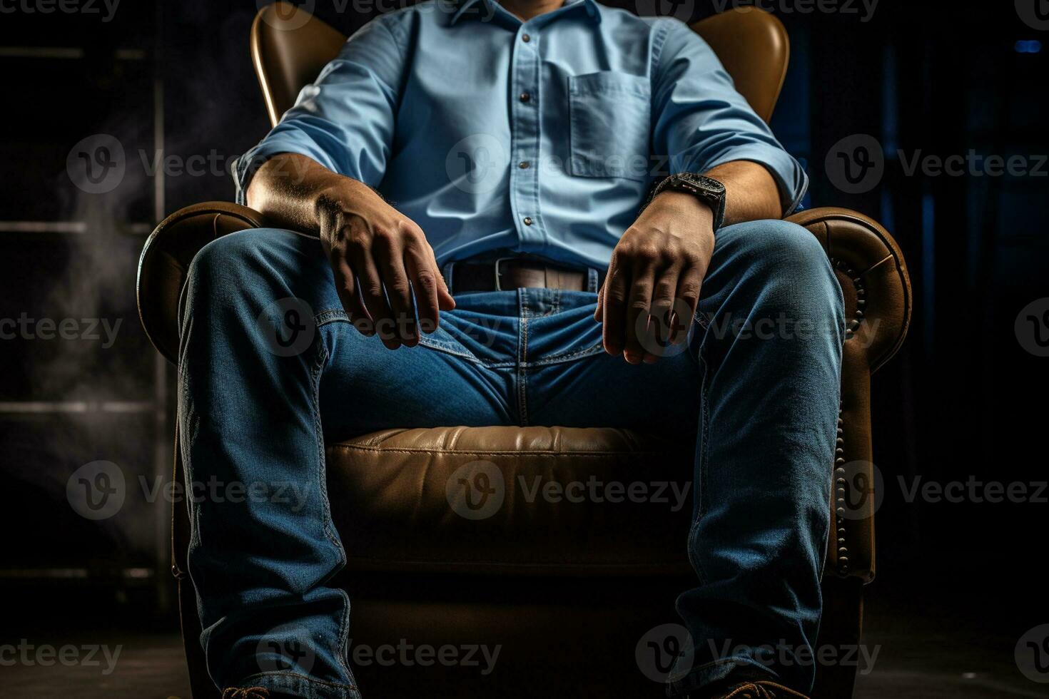 Handsome man wearing jeans sitting in a dark chair with a spotlight photo