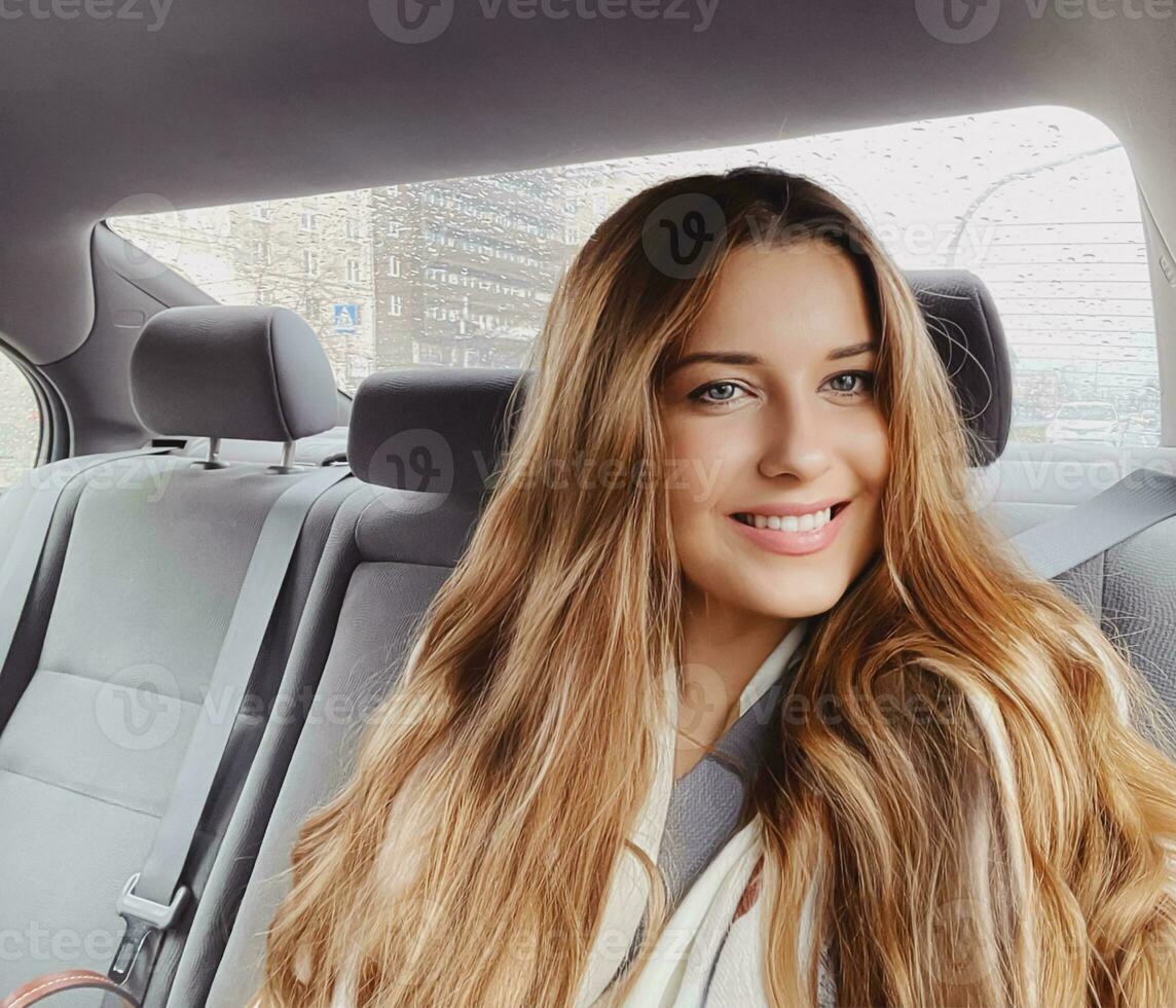 Young woman with long hair, wavy hairstyle in the car or taxi cab as passenger, exploring the city, transport and travel photo
