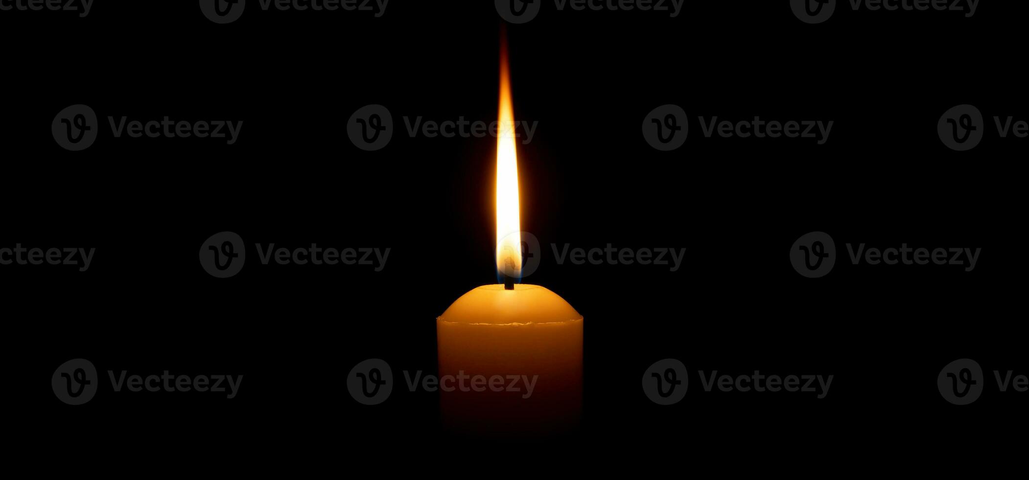 Single burning candle flame or light glowing on a big yellow candle on black or dark background on table in church for Christmas, funeral or memorial service with copy space. photo
