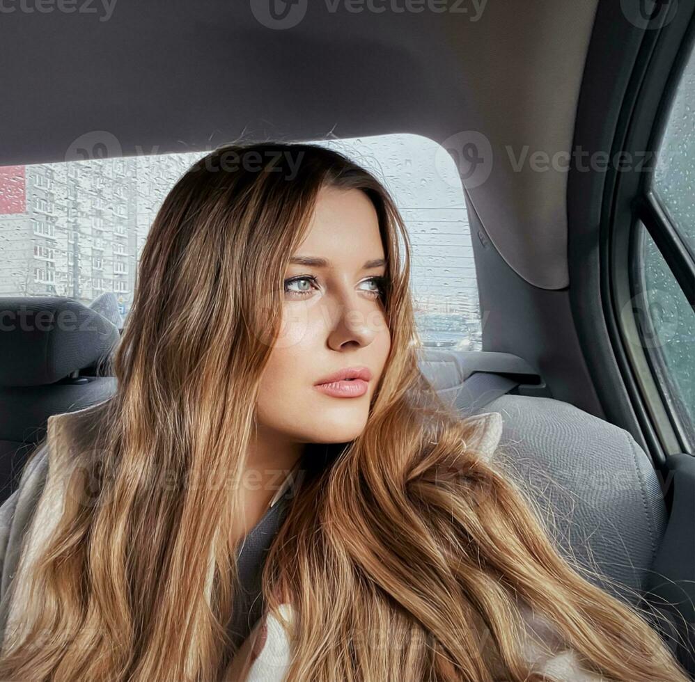 Young woman with long hair, wavy hairstyle in the car or taxi cab as passenger, exploring the city, transport and travel photo