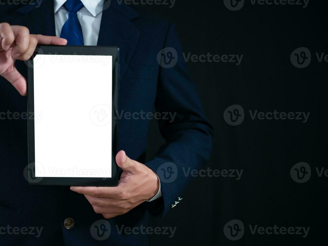 Businessman standing holding white screen tablet on dark background. Advertising concept. Banner sign. photo
