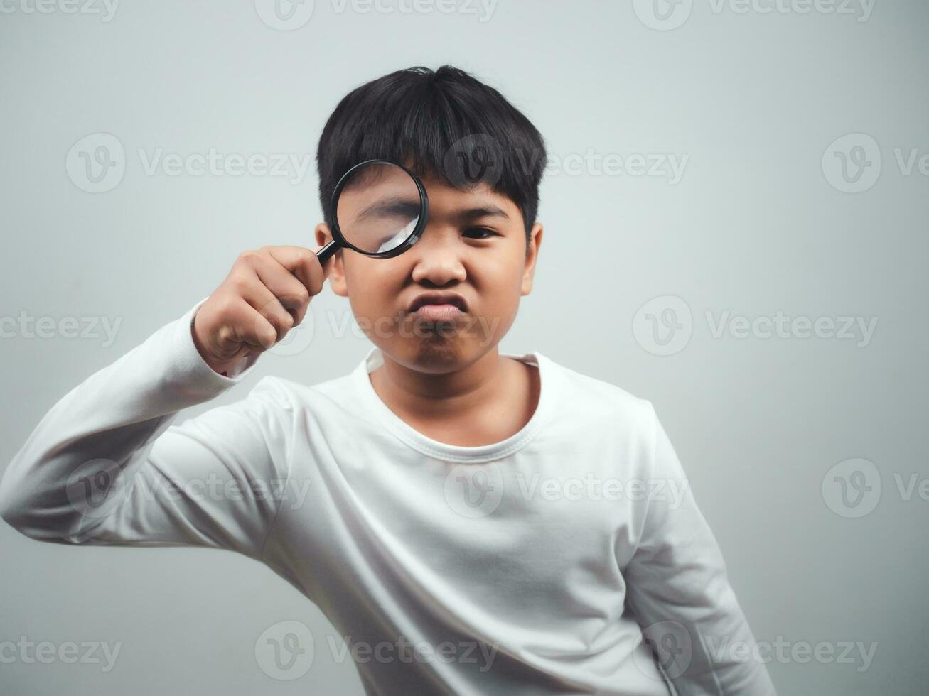 A boy wearing a white long-sleeved shirt is holding a magnifying glass on a white background. photo
