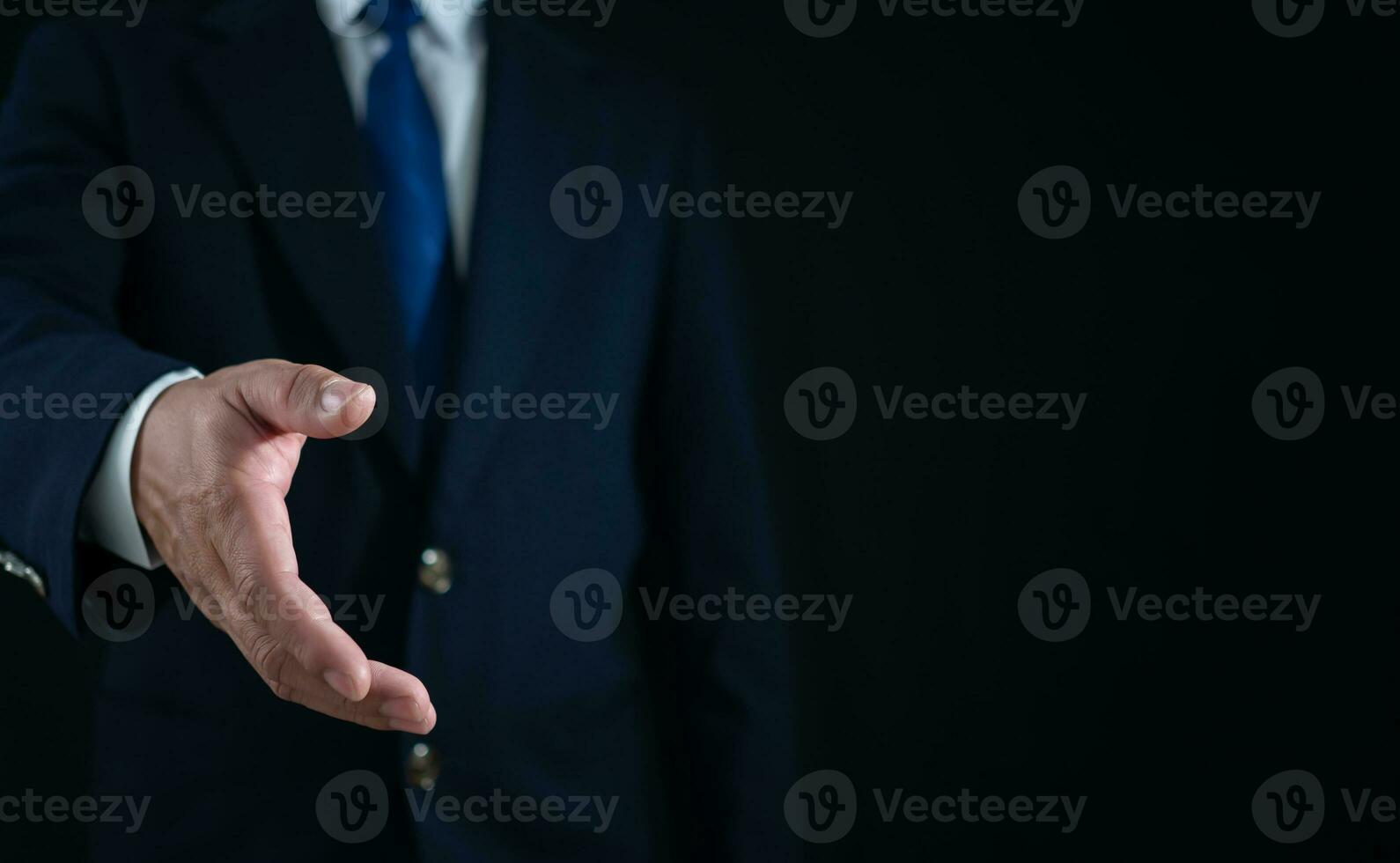 Businessman standing and doing handshake gesture on dark background. Business concept. Copy space. photo