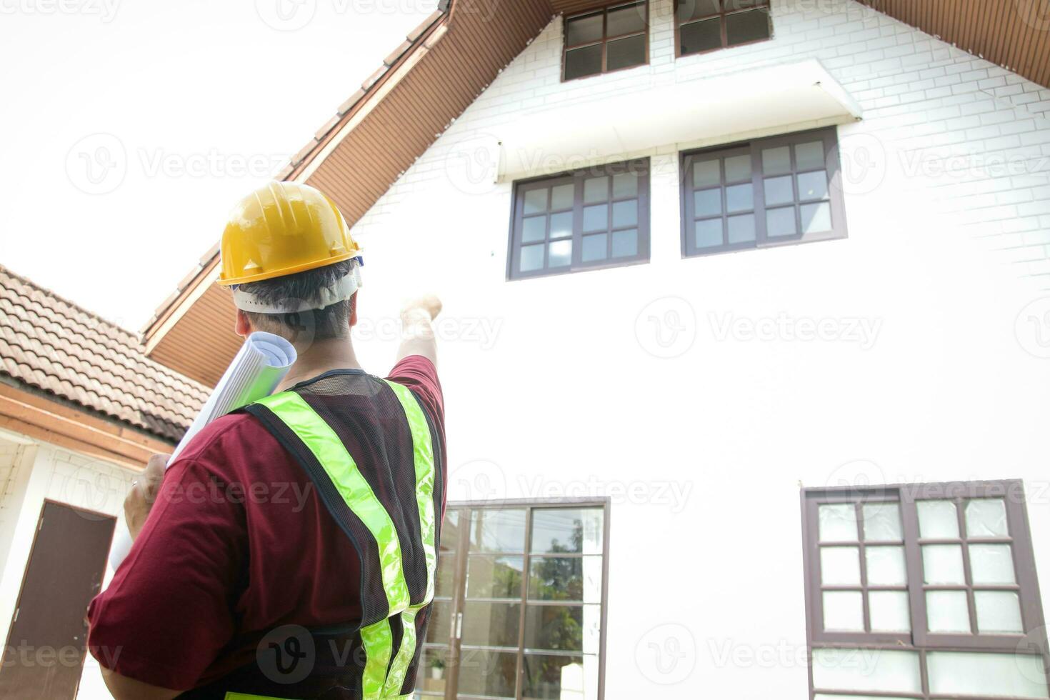 un masculino ingeniero inspecciona el casa a entregar eso a el cliente. en pie en frente de el casa, señalando a el frente. concepto de casa construcción residencial edificio foto