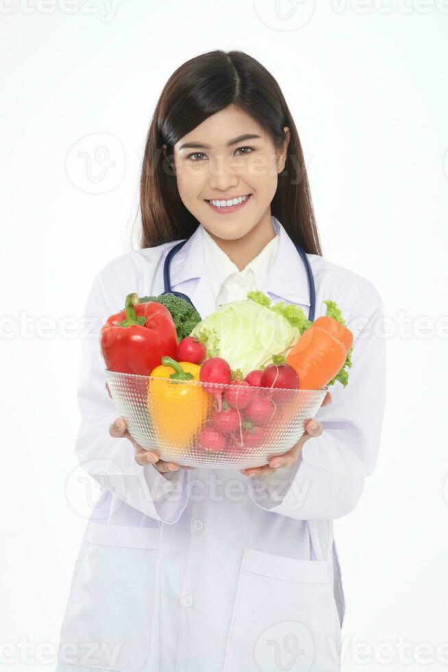 Beautiful young Asian female doctor has a beautiful smile. Holding a bowl of fresh organic vegetables Food for good health. Prescription food nutrition concept, healthy eating. White background. photo