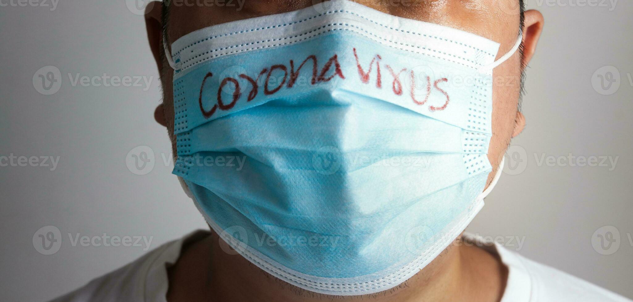 A fat Asian man wearing a blue mask writes the word Coronavirus. Concept of prevention of COVID-19 Social spacing prevents the spread of the virus, taking care of obese people. photo