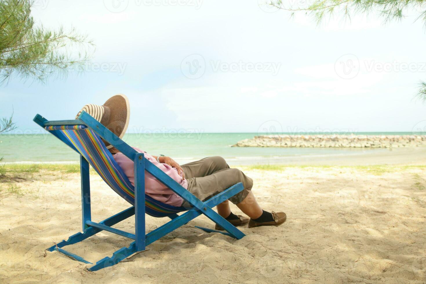 Asian old woman wearing a sun hat Lie down on a deck chair by the beach. Concept of natural tourism of the elderly during retirement age. Copy Space photo