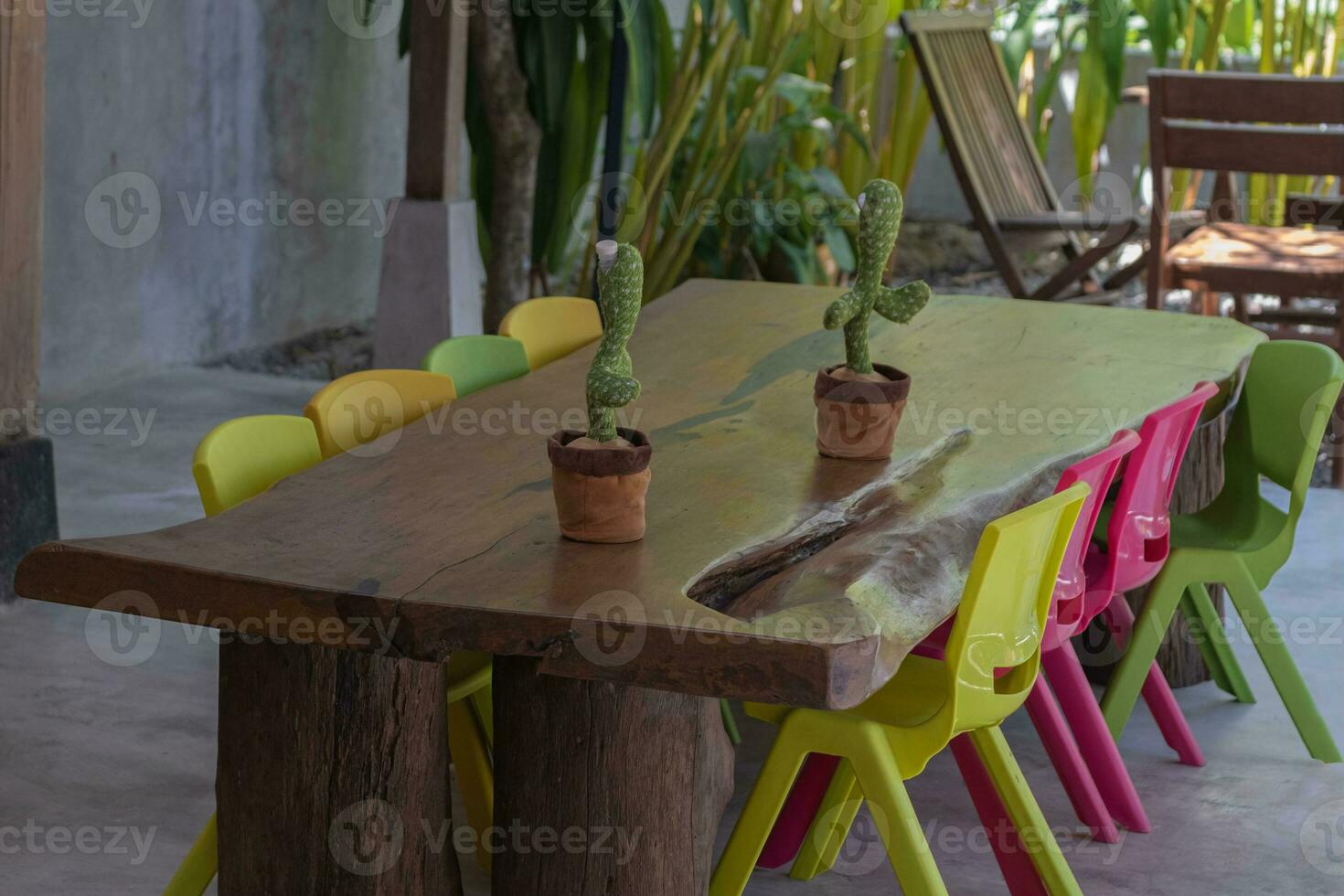 Colorful chairs are arranged around a table made of solid wood with a stuffed cactus swaying on top. photo