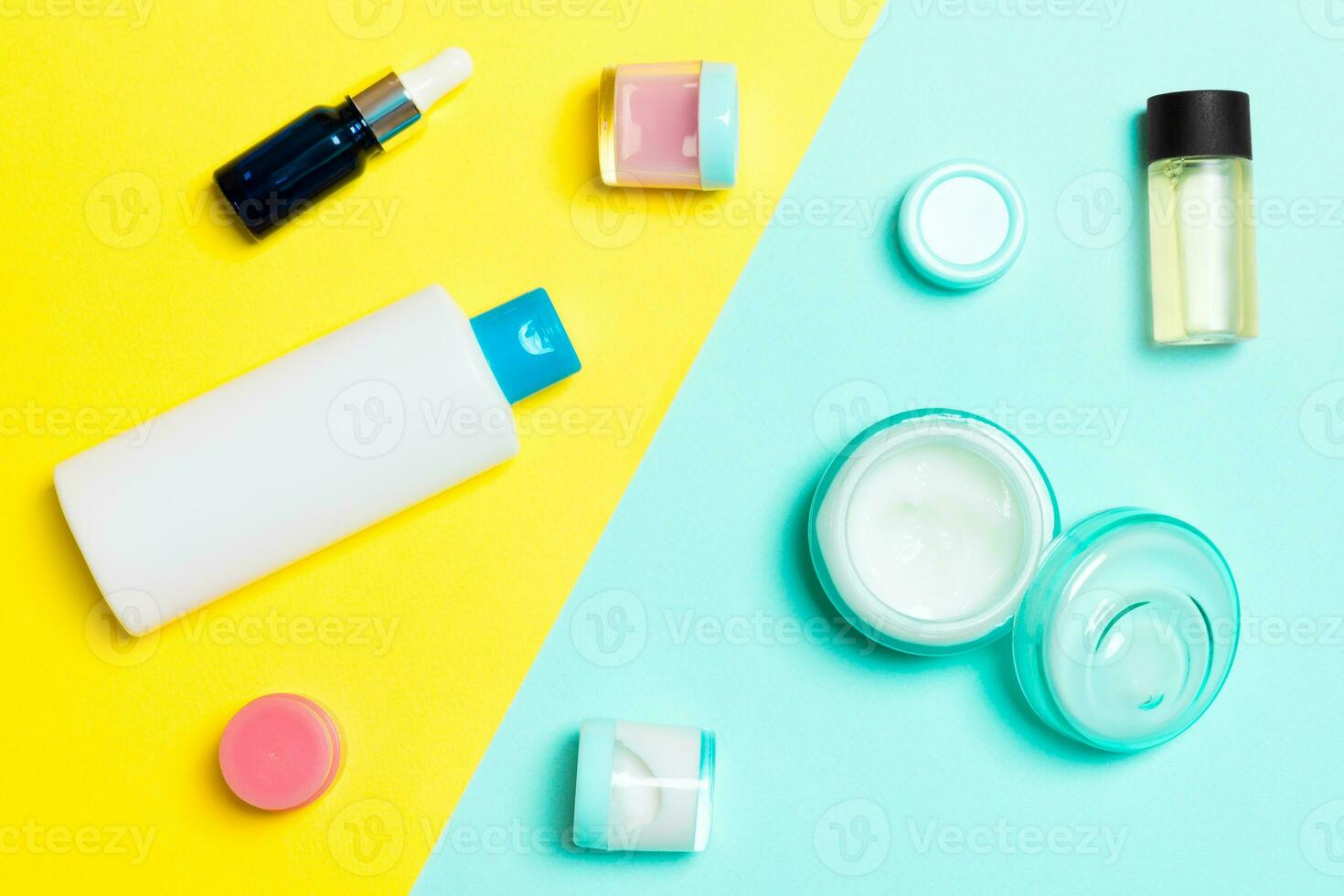 Top view of cosmetic containers, sprays, jars and bottles on yellow and blue background. Close-up view with empty space for your design photo