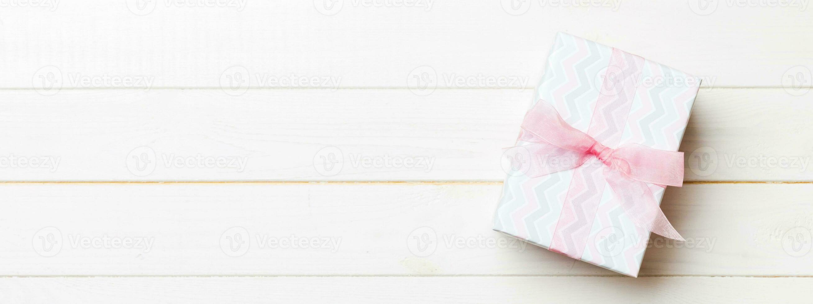 Beautiful gift box with a colored bow on the white wooden table. Top view banner with copy space for you design photo