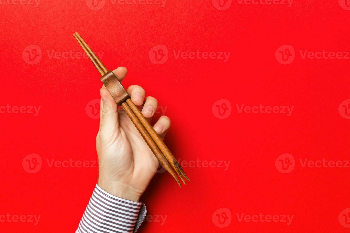 Cropped image of male hand holding chopsticks on red background. Asian food concept with copy space photo