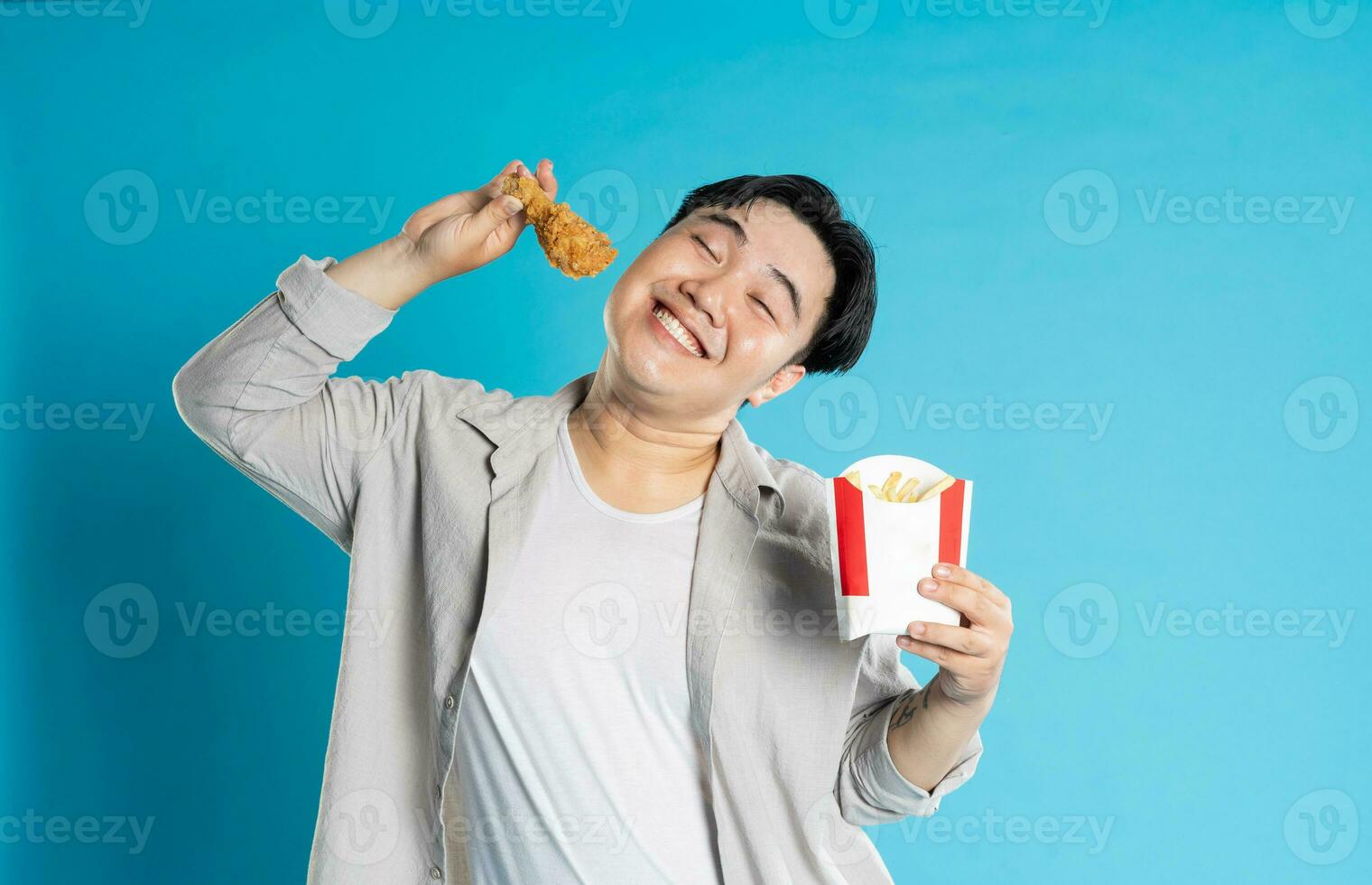 Portrait of asian man eating fast food on blue background photo