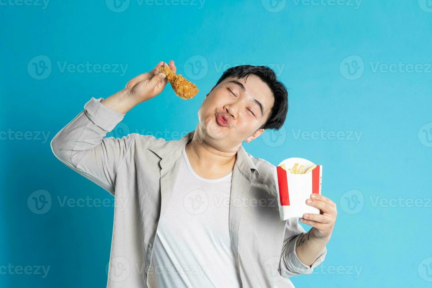 Portrait of asian man eating fast food on blue background photo