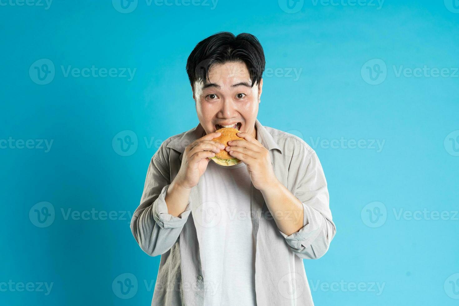 Portrait of asian man eating fast food on blue background photo