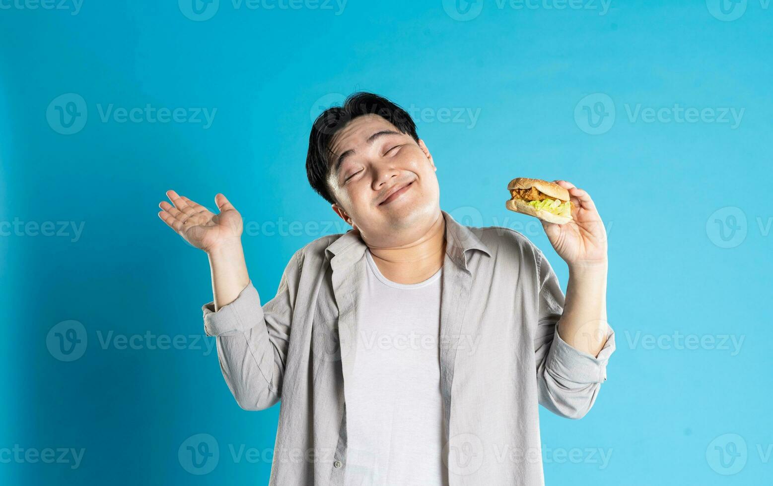 Portrait of asian man eating fast food on blue background photo