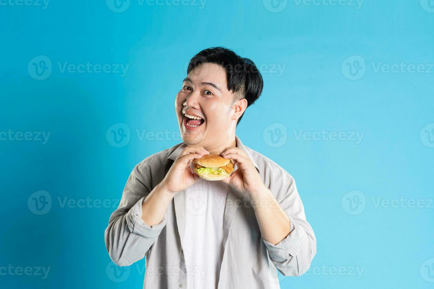 Portrait of asian man eating fast food on blue background photo