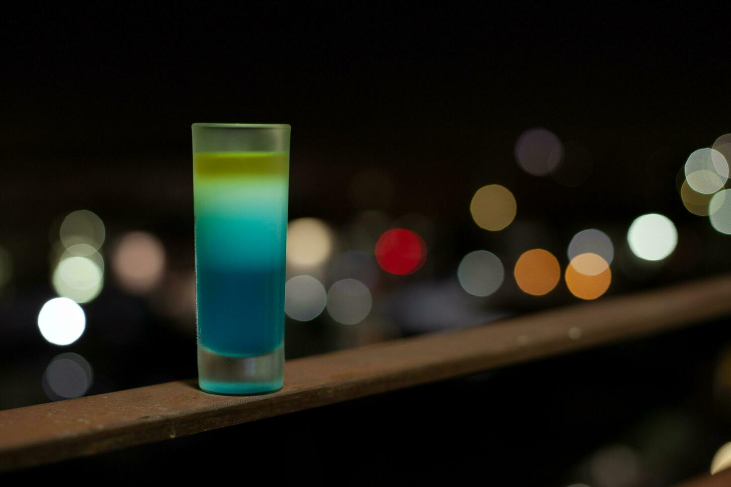 Cocktail shot glass placed on iron railing against bokeh light background. photo