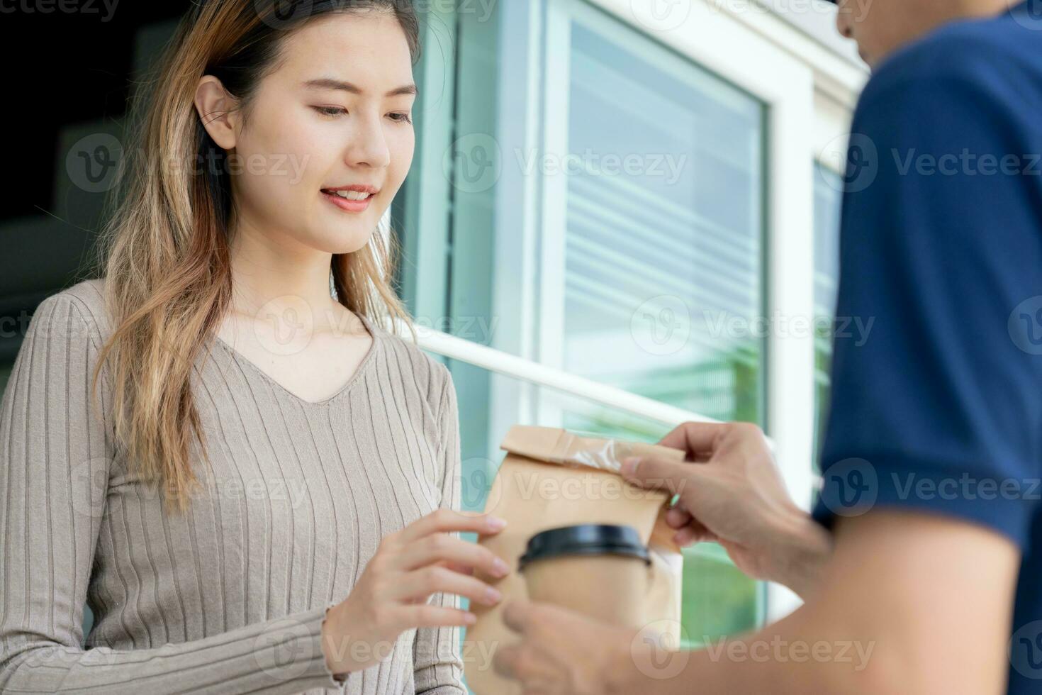 Happy smiling Asian woman receives paper box parcel of food from courier front house. Delivery man send deliver express. online shopping, paper container, takeaway, postman, delivery service, packages photo